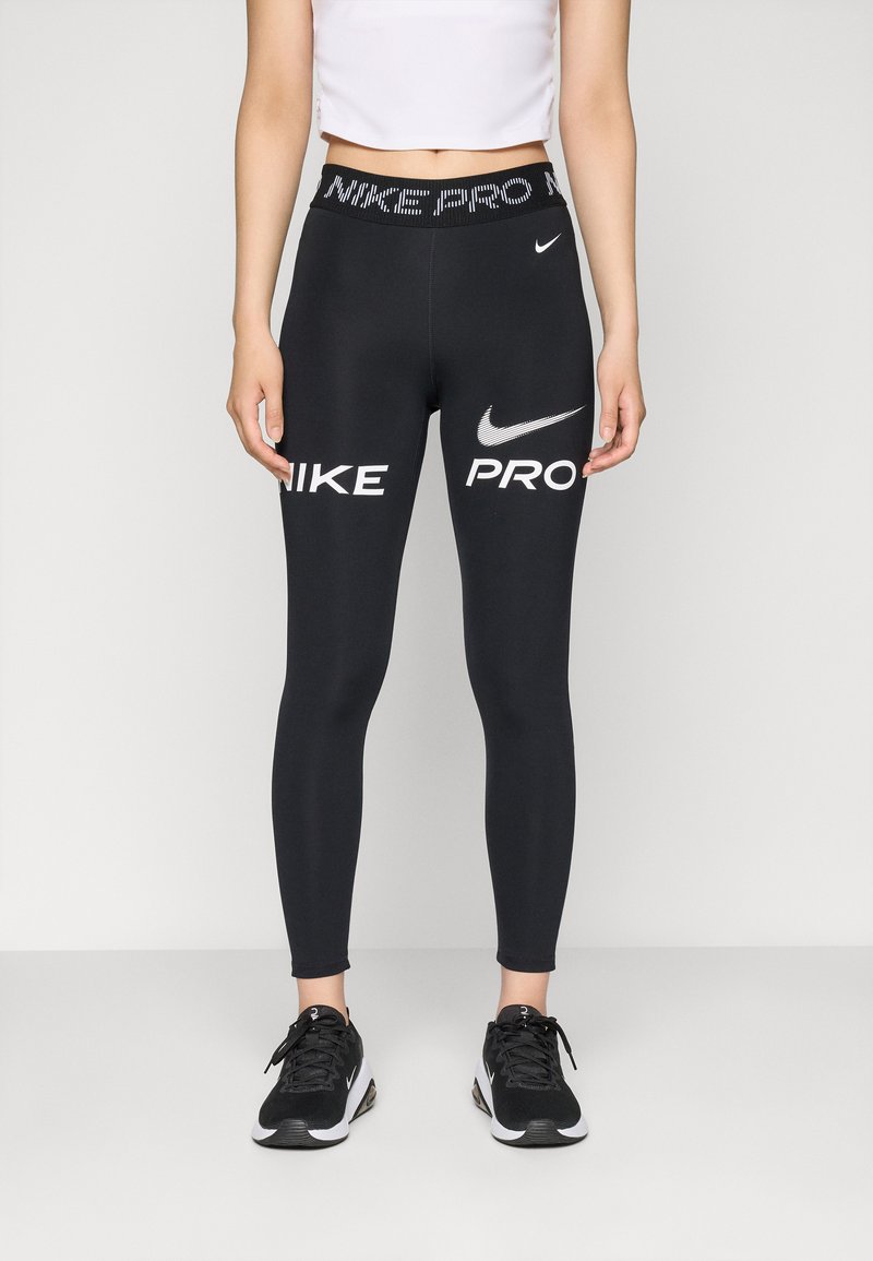 Schwarze Nike Pro Leggings mit weißen Logo- und Textakzenten. Hoher Bund, glattes Material, figurbetonte Form, kombiniert mit schwarzen Sportschuhen.