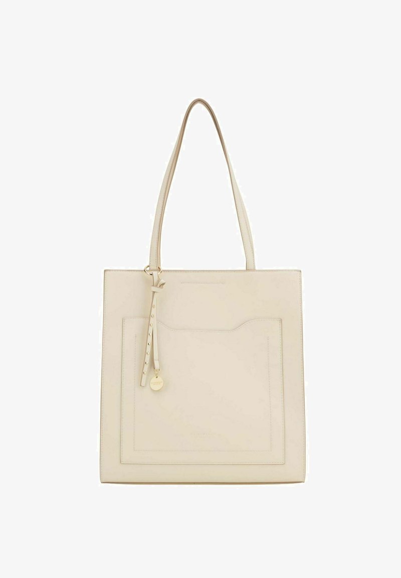 Sac fourre-tout beige clair en cuir avec deux longues anses, une poche avant et un détail de sangle ornée d'un charm rond en or.