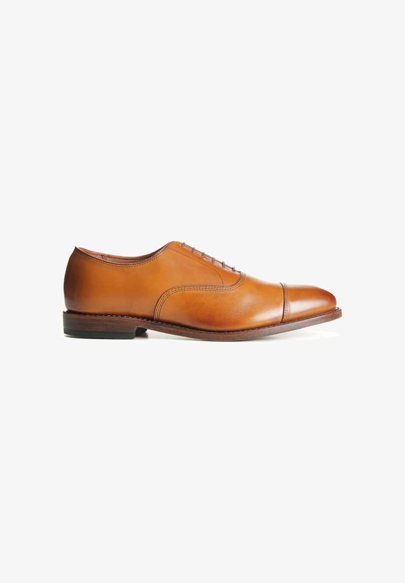 Chaussure de ville en cuir tan avec un embout, présentant une finition lisse, six œillets et un petit talon en bois. Silhouette classique et épurée.