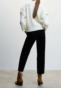 Pull blanc en tricot à manches courtes, associé à un pantalon en velours côtelé noir et des bottines à talons brunes. Texture lisse, design moderne.