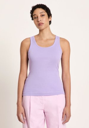 Woman wearing a sleeveless lavender tank top and high-waisted light pink pants against a plain light background.