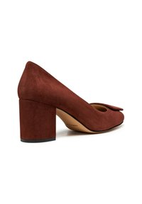 Zapato de tacón bloque de ante marrón con punta redondeada y detalle de lazo en la parte delantera. Presenta un tacón grueso para mayor estabilidad y un forro interior suave.