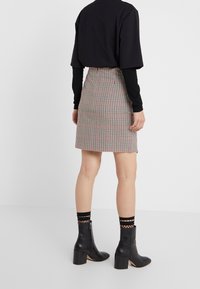 Jupe mini à carreaux au design ajusté, présentant des teintes de crème, rouge et noir. Portée avec des bottines noires et des chaussettes à motifs.