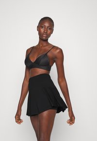 Zwarte bh met een gestructureerd ontwerp, voorzien van dunne bandjes en een v-hals, gecombineerd met een zwarte flared skort met een elastische tailleband.