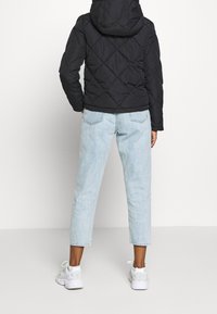 Černá prošívaná bundy s kapucí, kterou modelka kombinuje s světle modrými zkrácenými džíny. Nosí bílé tenisky a stojí s otočeným zády.