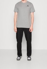Camiseta de algodón gris con logo negro de Jordan, combinada con pantalones cargo negros con bolsillos laterales y zapatillas negras y blancas.