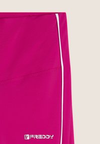Leggings de sport rose fabriqués en tissu extensible. Dotés de passepoils blancs sur les côtés et d'un petit logo argenté en bas. Texture lisse.