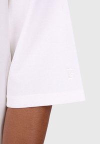Hvid bomulds T-shirt med rund hals, korte ærmer og et broderet bogstav "B" på kanten. Blød tekstur og enkelt design.