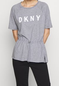 Top corto de manga corta gris con "DKNY" impreso en blanco. Cuenta con una cintura con cordón, aberturas laterales y un ajuste relajado. Fabricado con una tela ligera.