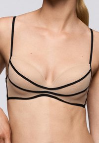 Nude mesh bralette met zwarte afwerking. Ontwerp met zachte cups, dunne verstelbare bandjes en gebogen lijnen op de cups voor een moderne uitstraling.