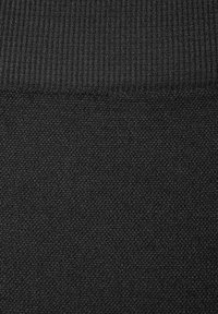 Tumma musta tekstiili, jossa on raidoitettu yläosa ja alempi osa hienolla, teksturoidulla neulekuviolla.