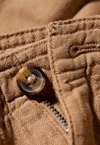 Brun tyg med en strukturerad väv, med en rund knapp med ett marmormönster och en synlig metallblixtlås längs kanten.