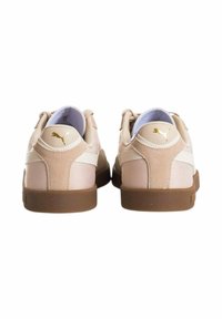 Zapatillas Puma que cuentan con una parte superior de un beige claro, materiales de ante y malla, franja lateral blanca y suela de goma marrón. Detalles del logo en dorado.
