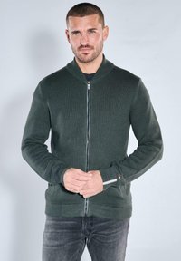 Dunkelgrüne Strickjacke zum Reißverschluss mit Bomber-Design. Verfügt über gerippte Bündchen und Saum, ein strukturiertes Muster und einen Metallreißverschluss.