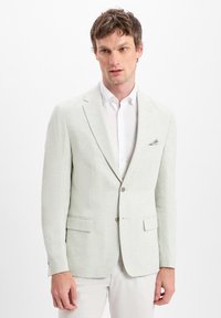 Helles graues Leinen-Blazer mit Reverskragen, zwei vorderen Taschen und einem einzigen Knopfverschluss. Getragen über einem weißen Kragenhemd.