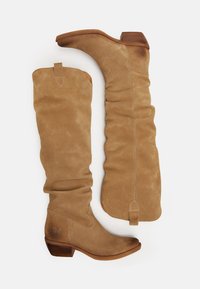 Bottes en daim beige jusqu'au genou avec un design plié, un talon empilé, un bout arrondi et des coutures proéminentes. Comprend une languette pour un enfilage facile.