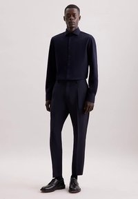 Camicia a maniche lunghe blu navy con colletto classico e abbottonatura sul davanti, abbinata a pantaloni sartoriali a vita alta. Tessuto liscio, design elegante.