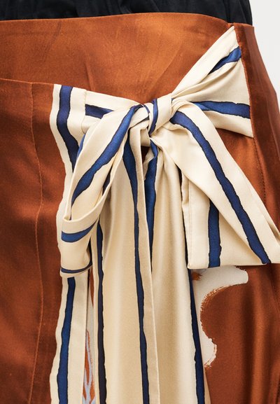 Κοντινή λήψη καφέ φούστας με μεγάλο μπεζ φιόγκο δεμένο στη μέση, με κάθετες μπλε και καφέ ρίγες στο φιόγκο.