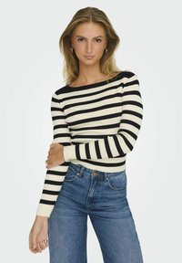 Svart och krämrandig ribbad tröja med båturringning, åtsittande långärmar och kontrasterande mudd, kombinerad med högmidjade blå jeans.
