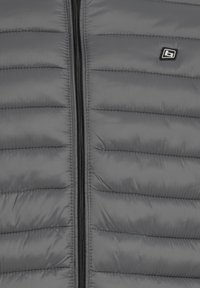 Hall triibuline jope vertikaalse musta tõmblukuga ja väike must-valge logoplaat paremal ülaserval.