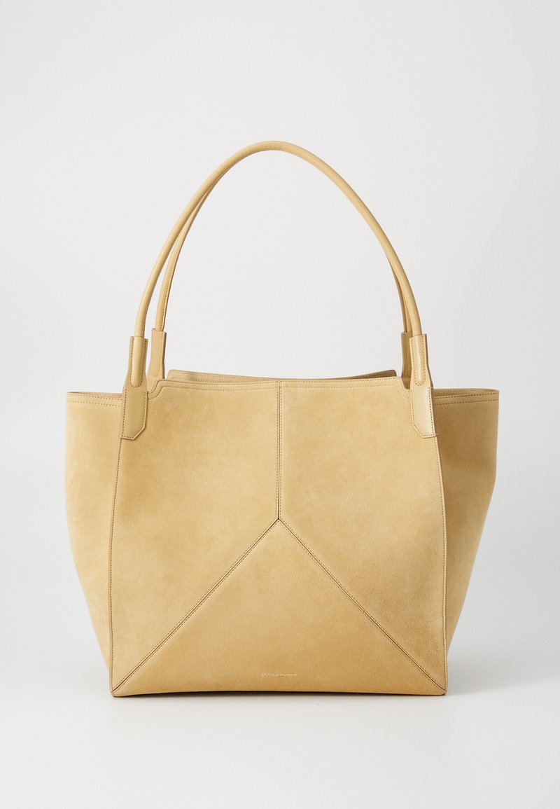 Beige suede tote bag with two rounded handles, a triangular design on the front, and subtle stitching details. Smooth, soft texture.