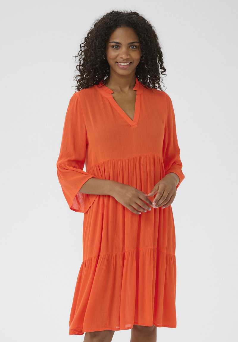 Robe orange vif avec une coupe décontractée, dotée d'un décolleté en V, de manches longues évasées et d'une jupe à volants. Tissu léger et texturé.