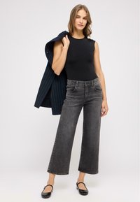 Sort ærmeløs bodysuit parret med højtsiddende, vidde ben, falmede sorte jeans. En marineblå stribet blazer hænger over skulderen.