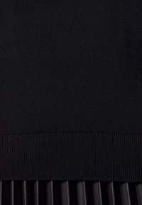 Schwarzer Pullover mit geripptem Saum, kombiniert mit einem unteren Teil aus plisseeartigem schwarzem Stoff. Glatte Textur ohne Muster oder sichtbare Beschläge.