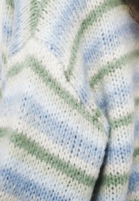Primer plano de tela tejida suave con rayas en forma de espiga en azul, verde y blanco y una textura difusa.
