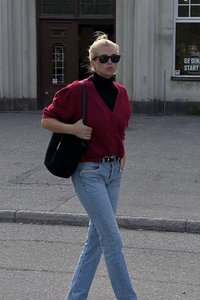 Raudona megzta kardiganas su trumpomis rankovėmis, juoda golfo tipo marškinėliai, šviesiai mėlynos džinsai ir juoda rankinė; vaikščiojimas lauko aplinkoje.
