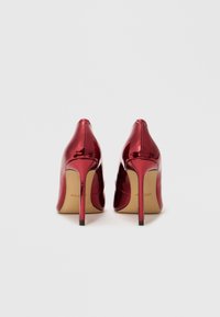 Røde lakk lær høye hæler med spiss tå, 10 cm stiletto hæler og en glatt, blank overflate. Svart akcent på hæltuppene.