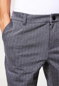 Pantalones gris con rayas finas hechos de tela ligera, con bolsillos laterales y cierre delantero de cremallera, con un botón en la pretina.