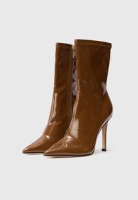 Brązowe lakierowane botki za kostkę z szpiczastym noskiem, obcasem w stylu stiletto i bocznym zamkiem błyskawicznym, charakteryzujące się gładką, błyszczącą teksturą.