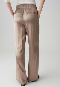 Wijdvallende broek in een zachte, glanzende taupe stof. Voorzien van een elastische tailleband en twee achterzakken met subtiele afwerking.