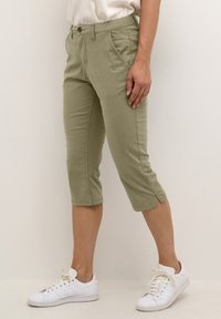 Kratke khaki hlače s ravnim krojem, sprednjimi žepi in gumbnim zapiranjem. Nosijo se z belimi supergami na nevtralni podlagi.