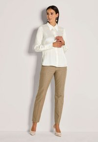 Crème blouse met een puntscollar en knopen aan de voorkant, gecombineerd met lichtbruine, textuurvolle broek en nude hakken. Eenvoudig, getailleerd design.
