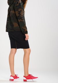 Camouflagejakke i mørkegrøn og brun, sort denimnederdel med lynlås foran og røde sneakers med hvide detaljer.