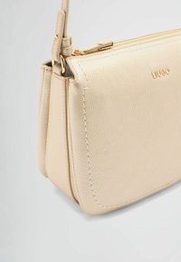 Borsa a mano in pelle beige con finitura testurizzata, caratterizzata da una cerniera e dettagli di cucitura in tono oro, forma compatta e tracolla removibile.