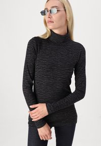 Zwarte coltrui met een gestructureerd zebra-patroon, lange mouwen en een aansluitend ontwerp, gecombineerd met minimalistische zonnebril en donkere jeans.