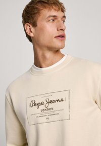 Felpa crema con collo rotondo e logo stampato che recita "Pepe Jeans London", caratterizzata da dettagli testurizzati e una vestibilità rilassata.
