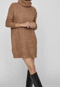 Abito a maglione marrone con collo alto, maniche lunghe, texture a coste e vestibilità rilassata, abbinato a stivali neri alti fino al ginocchio.