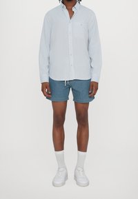 Světlomodrá košile s knoflíky a dlouhými rukávy, náprsní kapsa, džínové kraťasy, bílé tenisky a bílé kotníkové ponožky. Ležérní oblečení.