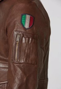 Manica di giacca in pelle marrone con una tasca con zip e un patch a forma di scudo della bandiera italiana sopra la tasca.