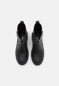 Botas de tobillo de cuero negro con un acabado suave, cremalleras laterales y puntas redondeadas. Suelas planas y diseño minimalista.