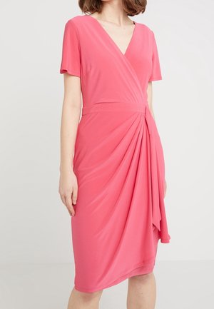 Kobieta nosząca koralowo-różową sukienkę kopertową do kolan z krótkimi rękawami i marszczonym detalem w talii.