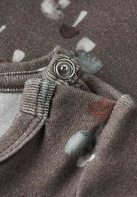 Jasnobrązowy materiał o miękkiej fakturze, z szarym zatrzaskiem i wielokolorowymi okrągłymi wzorami w odcieniach czerwieni i niebieskiego.