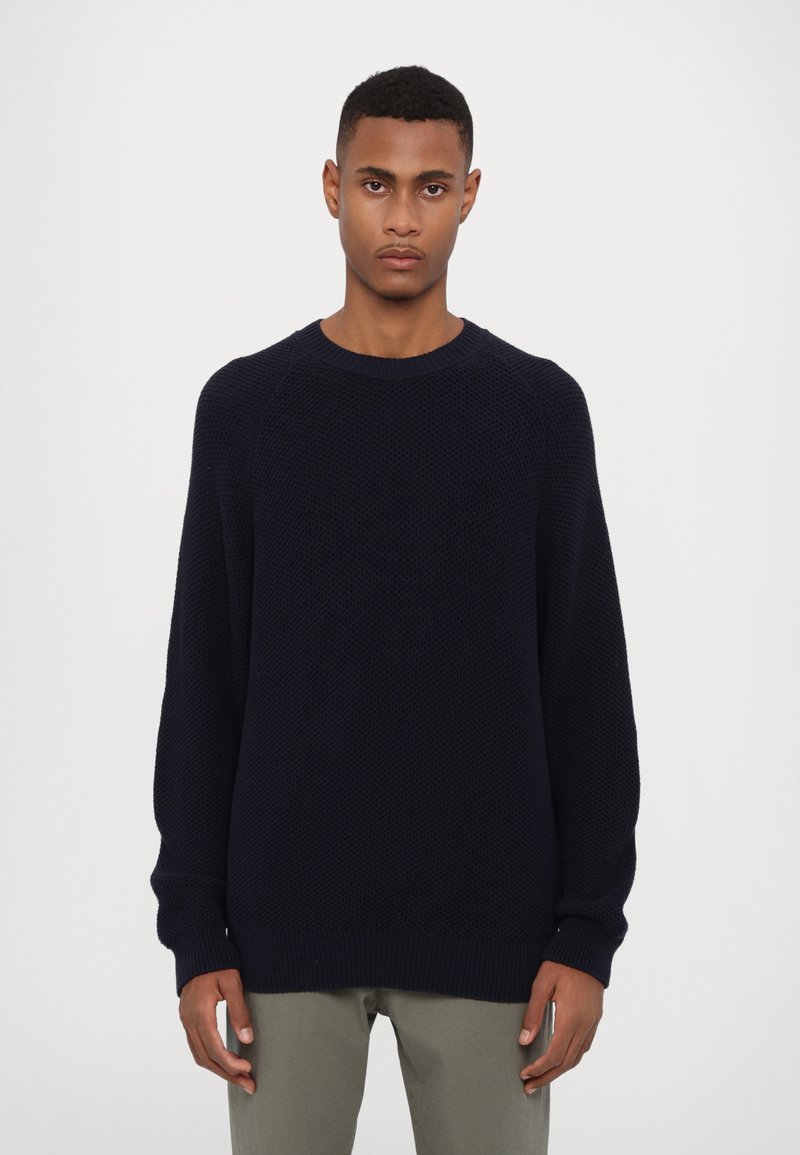 Pull en maille bleu marine avec un col rond côtelé et des manches longues, présentant un motif texturé et une coupe décontractée.