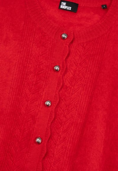 Rød strikket cardigan med ribbet halsudskæring, bølget knapræmme og sølvknapper med et tekstureret mønster på stoffet.