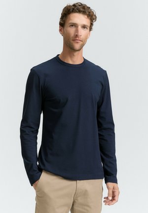 Camiseta de manga larga en color navy, fabricada en tejido suave, con cuello redondo y diseño ajustado, textura suave, combinada con pantalones de color beige claro. Sin patrones ni acentos visibles.