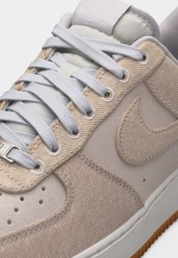 Μπεζ και ανοιχτού γκρι αθλητικό παπούτσι Nike με λευκά κορδόνια, υφασμάτινες λεπτομέρειες με υφή και εξωτερική σόλα από καουτσούκ gum που είναι ορατή στις άκρες.